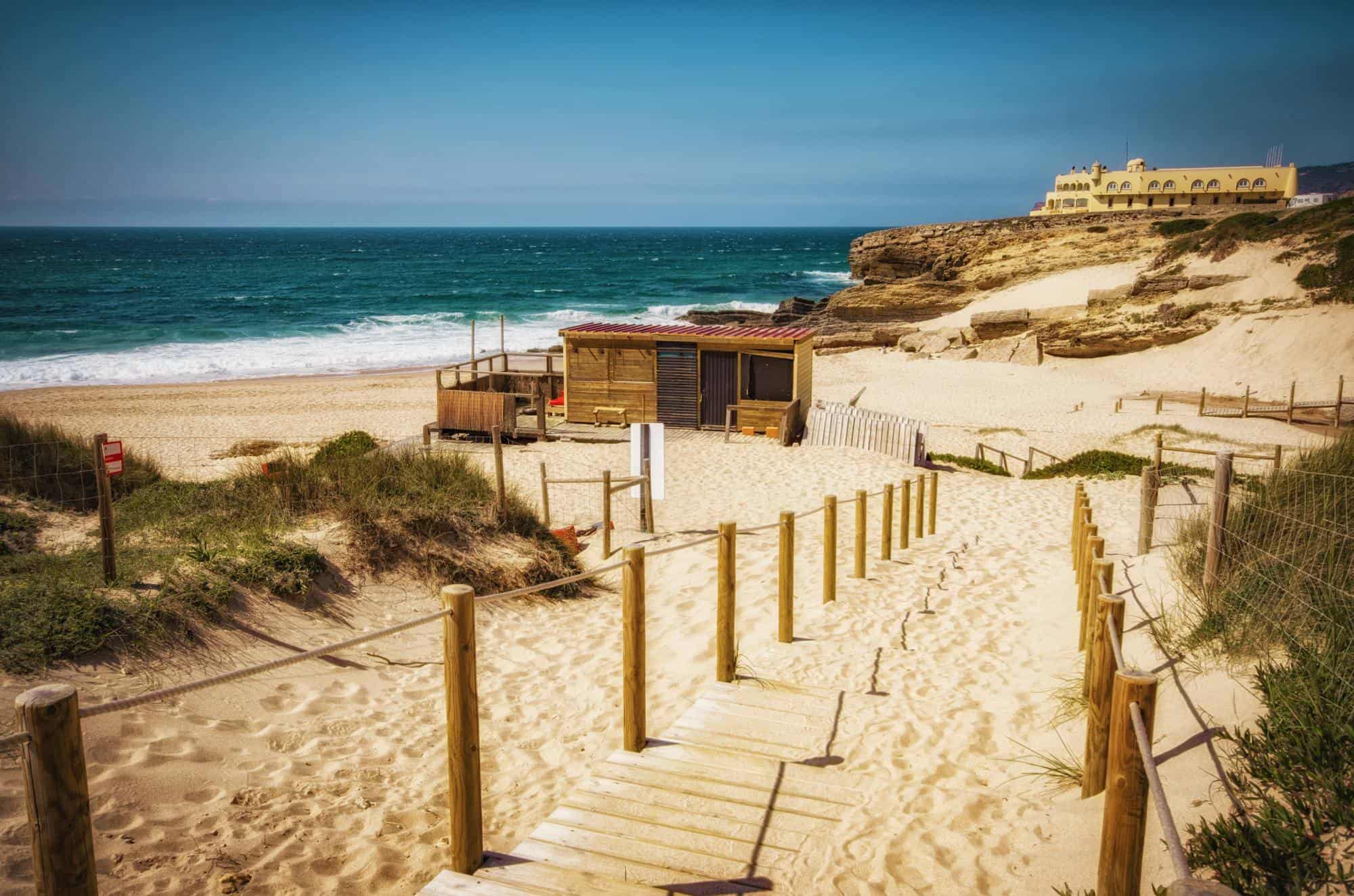 A long and sandy stretch of a coast near Cascais in Portugal, a wooden paved path leading to the beach