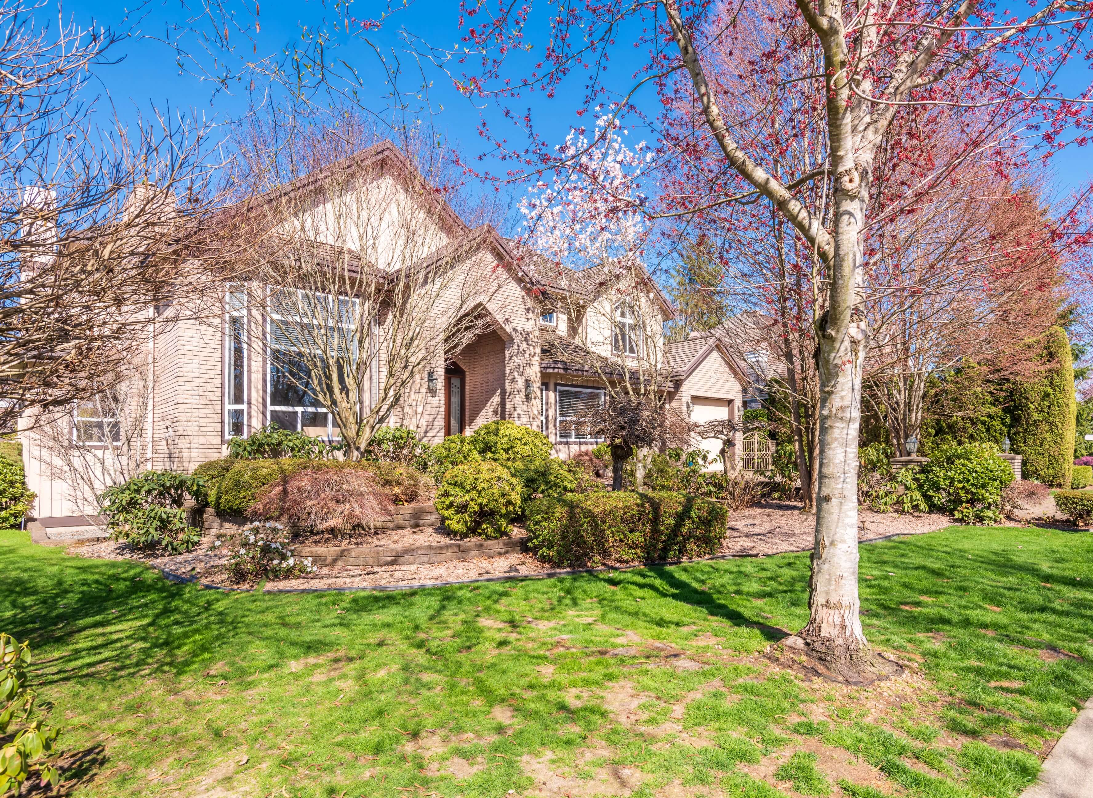 A detached house surrounded by a green garden and flowering trees in Kerrisdale, Vancouver