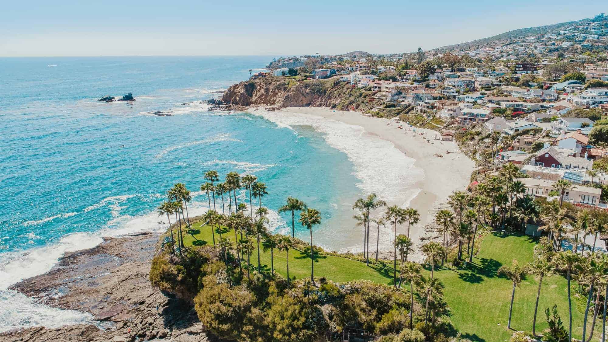 A small coastal city in California with a sandy beach, palms and emerald waters.