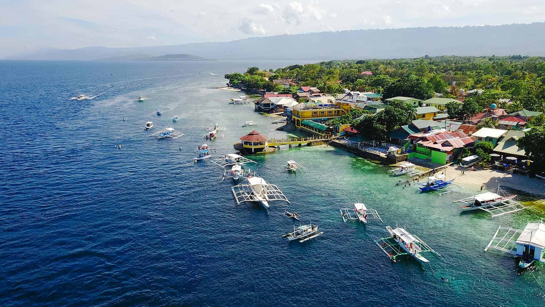 Philippines coastal views - blue calm waters, lush greenery, waterfront properties and traditional boats in the water.