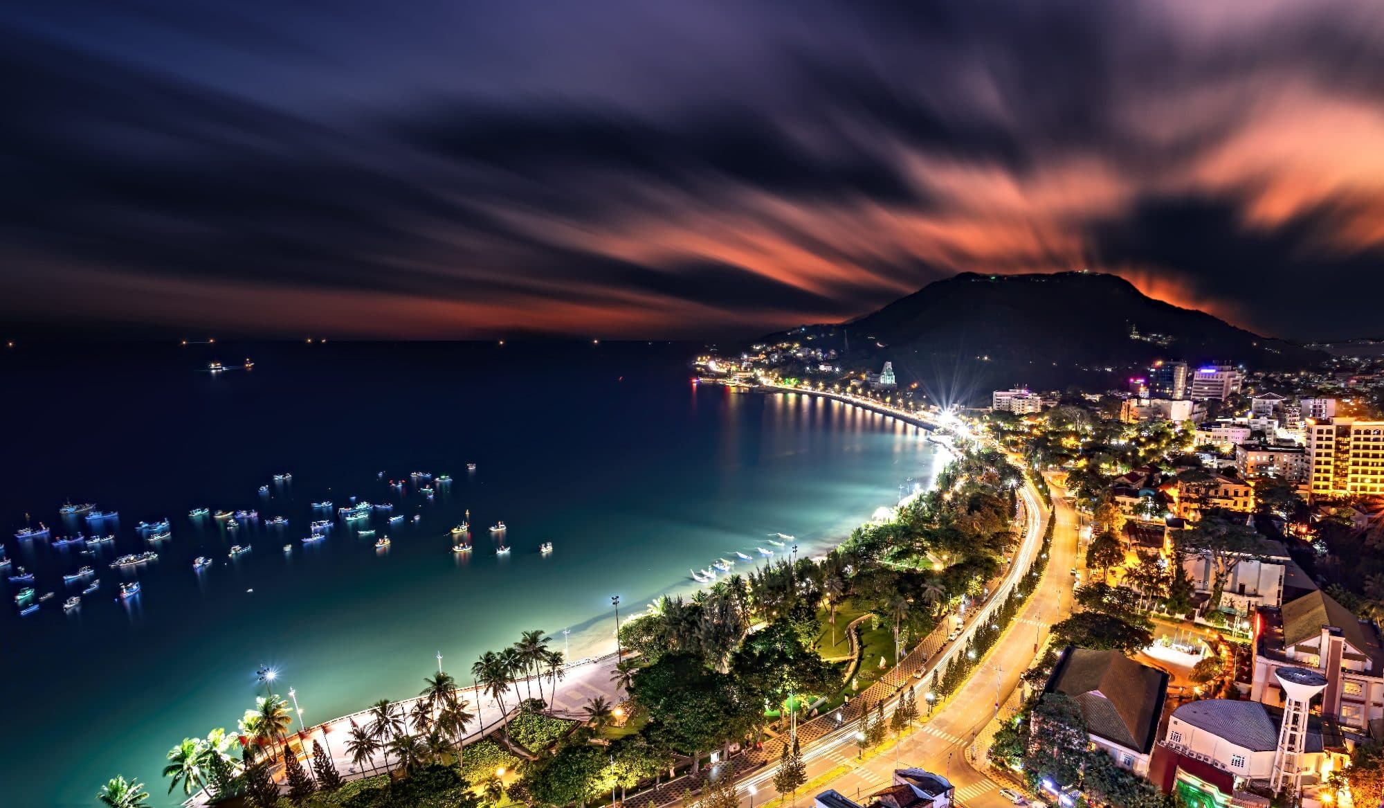 Panoramic coastal Vung Tau view from above, with waves, coastline, streets, coconut trees and Tao Phung mountain in Vietnam. Long exposure photography at night.